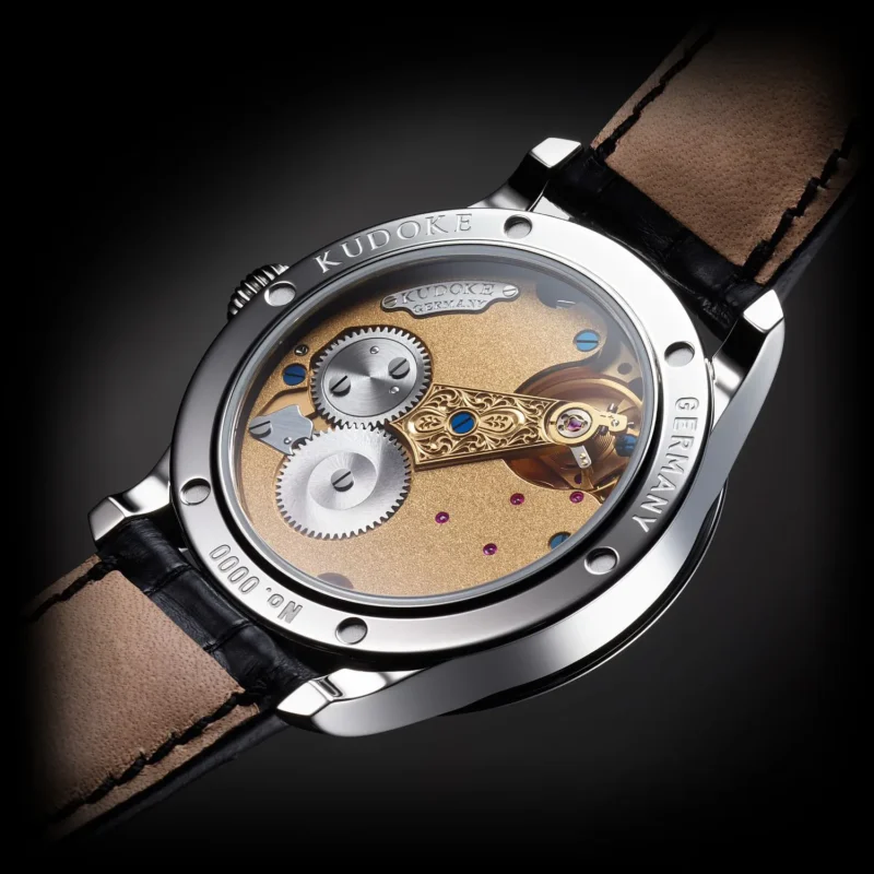 Kudoke 1 caseback showing in-house Kaliber 1 manual movement with hand-engraved balance cock and frosted finish